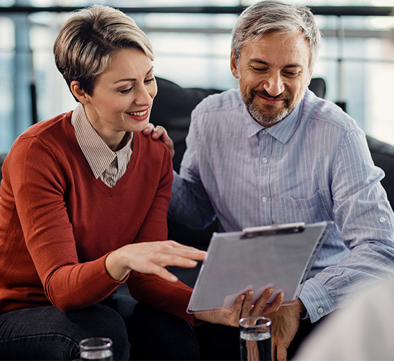 Refinancing consultation: middle-aged couple looking at a clipboard in an office.